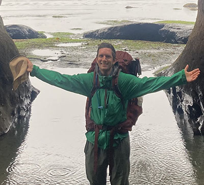 Jannes Koelling in hiking gear and backpack, arms spread wide while standing in rain and large puddles