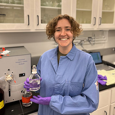 Stevie Walker standing in a lab wearing lab coat and holding bottle of liquid