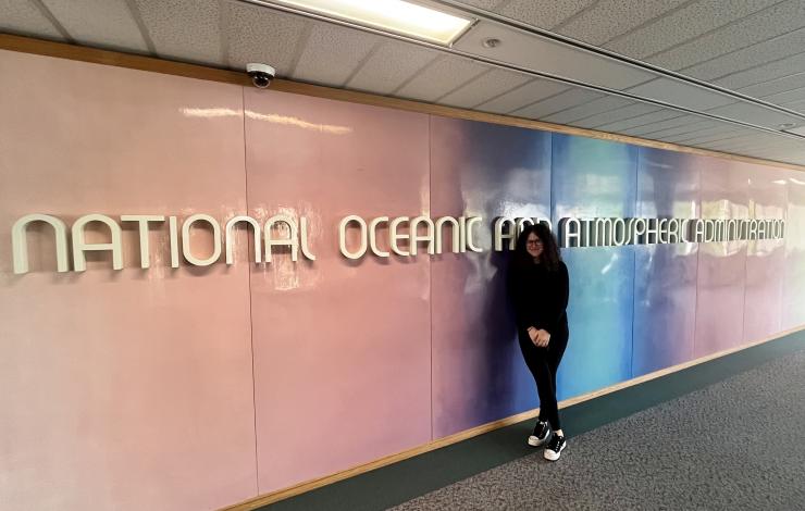 Chloe Rabinowitz standing in front of the NOAA sign at the NOAA Western Regional Office