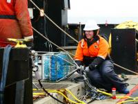 Shannon Brown on the sitting on the back deck of the NOAA Oscar Dyson connecting the automated eDNA sampler to the full mooring,