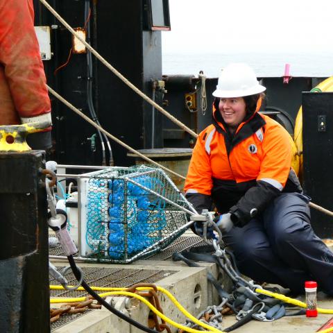 Shannon Brown sitting on the back deck of the NOAA Oscar Dyson connecting the automated eDNA sampler to the full mooring,