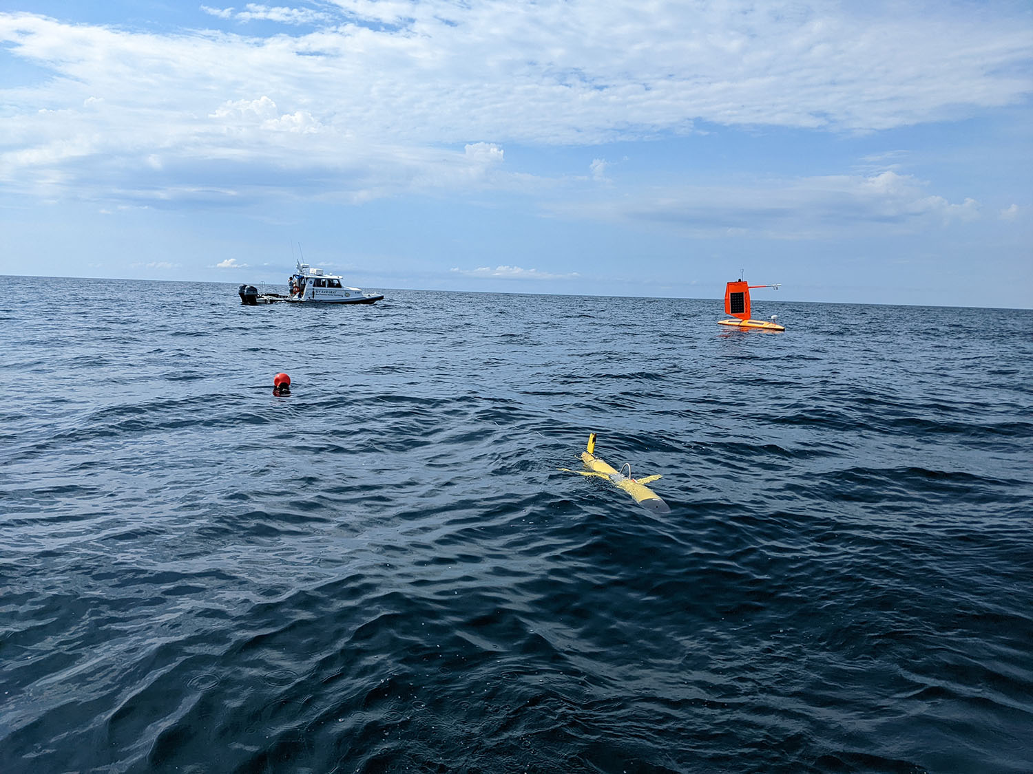 Saildrone meets ocean glider out in the water with boat in background