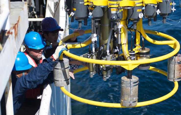 Two men who hard hats pull in a CTD rosette from the ocean. 