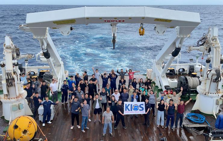 Group photo of 50 participants on the deck of the ship holding a KIOS banner 