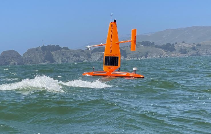 orange sailing drone in on the water with some waves sailing in front of San Francisco bluffs
