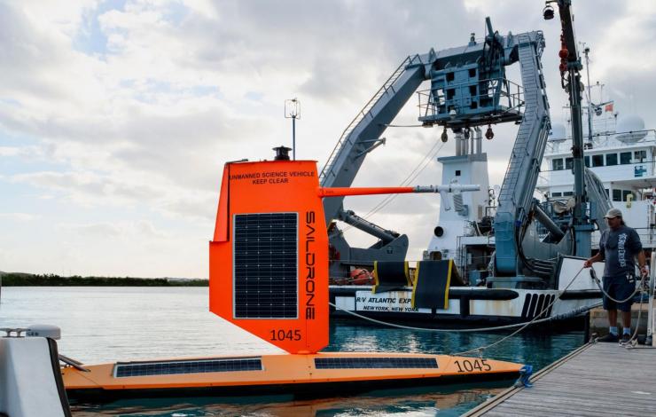 Saildrone 1045 in the water next to a ship, docked at a pier in Bermuda