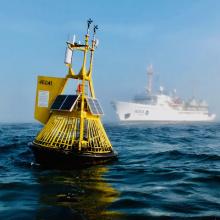 An yellow ocean acidification buoy located in the Pacific Ocean off the central Washington coast with the NOAA Ship Fairweather in the background. 