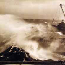 Sepia image of a ship and a destroyer encountering a large wave sweeping past the oiler's bow