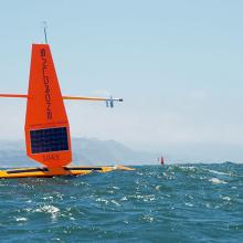 Two orange saildrones in the Pacific Ocean with San Francisco in the background. 