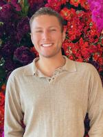 John smiling in front of flowers with beige shirt and short light brown hair